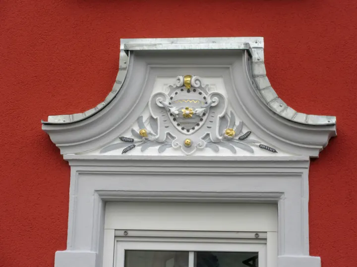 Stuckgiebel über dem Fenster einer roten Fassade